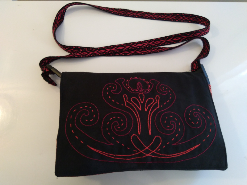 A black purse with an embroidered pattern on the front and a tablet woven strap
